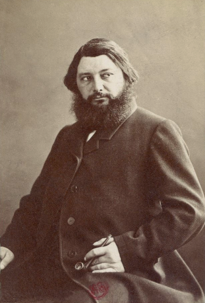 Black and white photograph of Gustave Courbet seated, with a full beard, dressed in a dark suit, holding a cigar, exuding confidence and contemplation.a Great French Realism artist born at Ornans